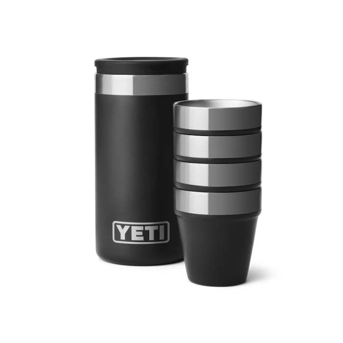 Four black stainless steel YETI shot glasses stacked next to a matching rugged carrying case on a white background.